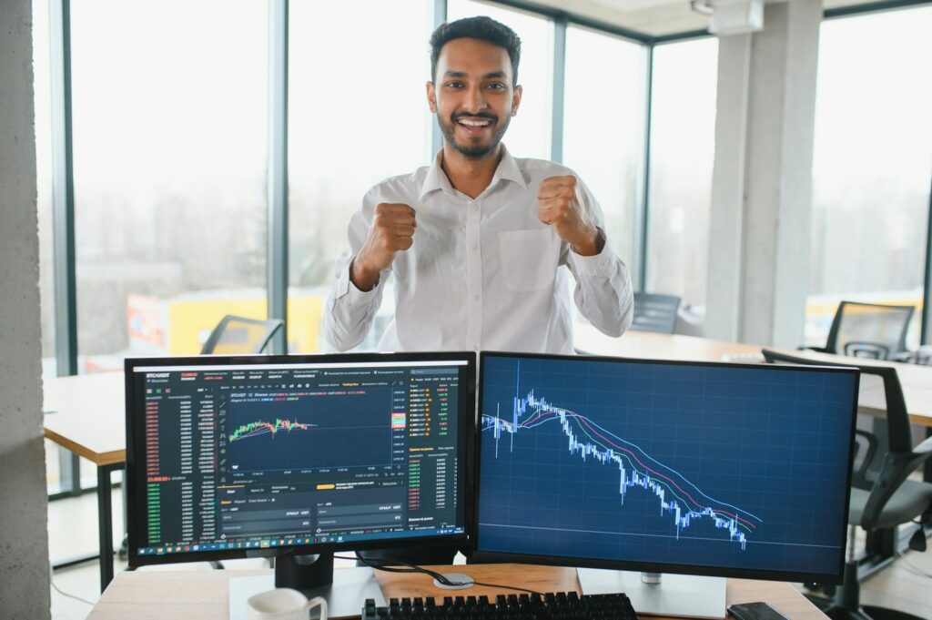 Young indian business man trader looking at computer screen with trading charts